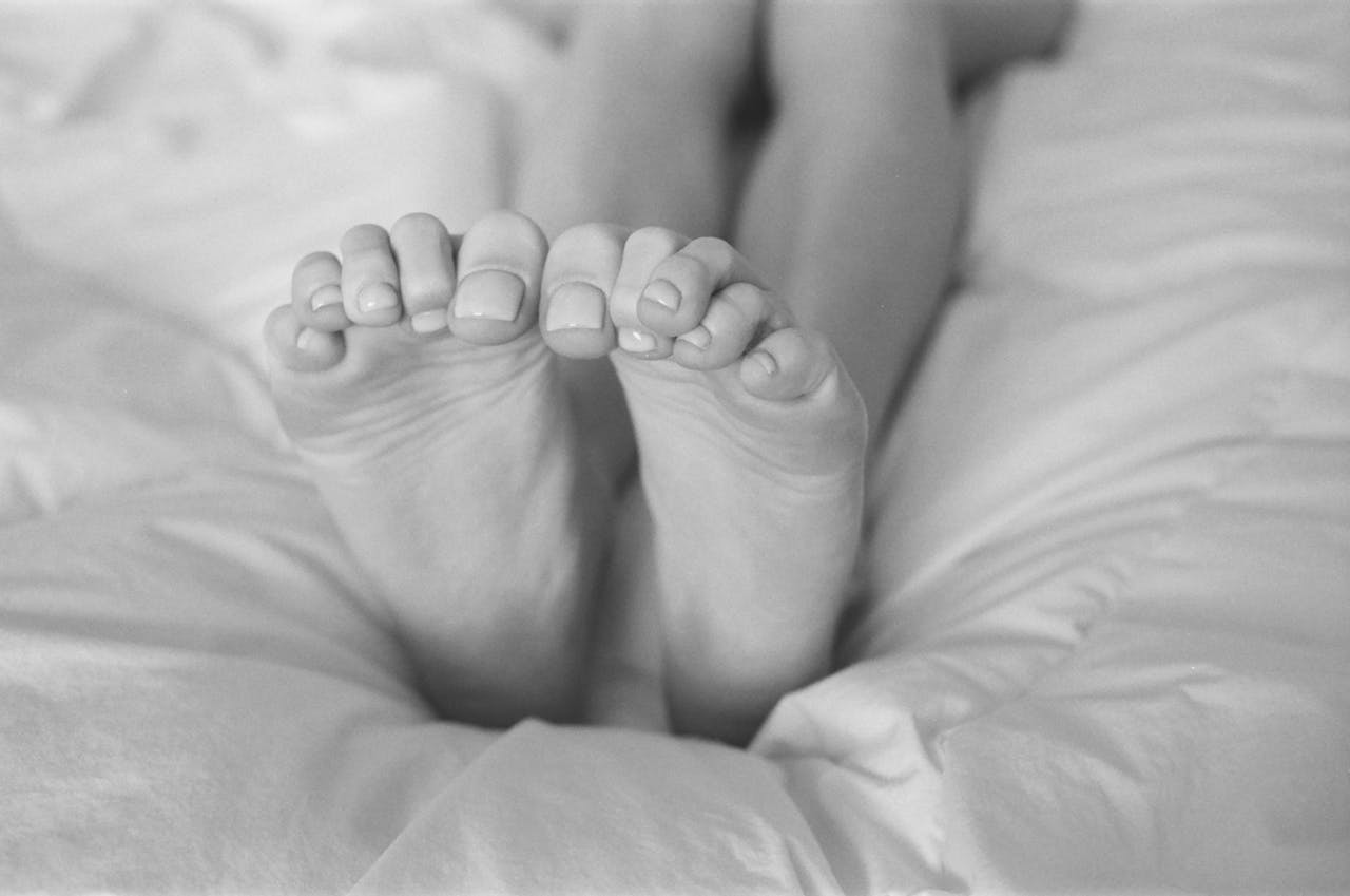 Monochrome close-up of bare feet on a cozy bed, showcasing relaxation.